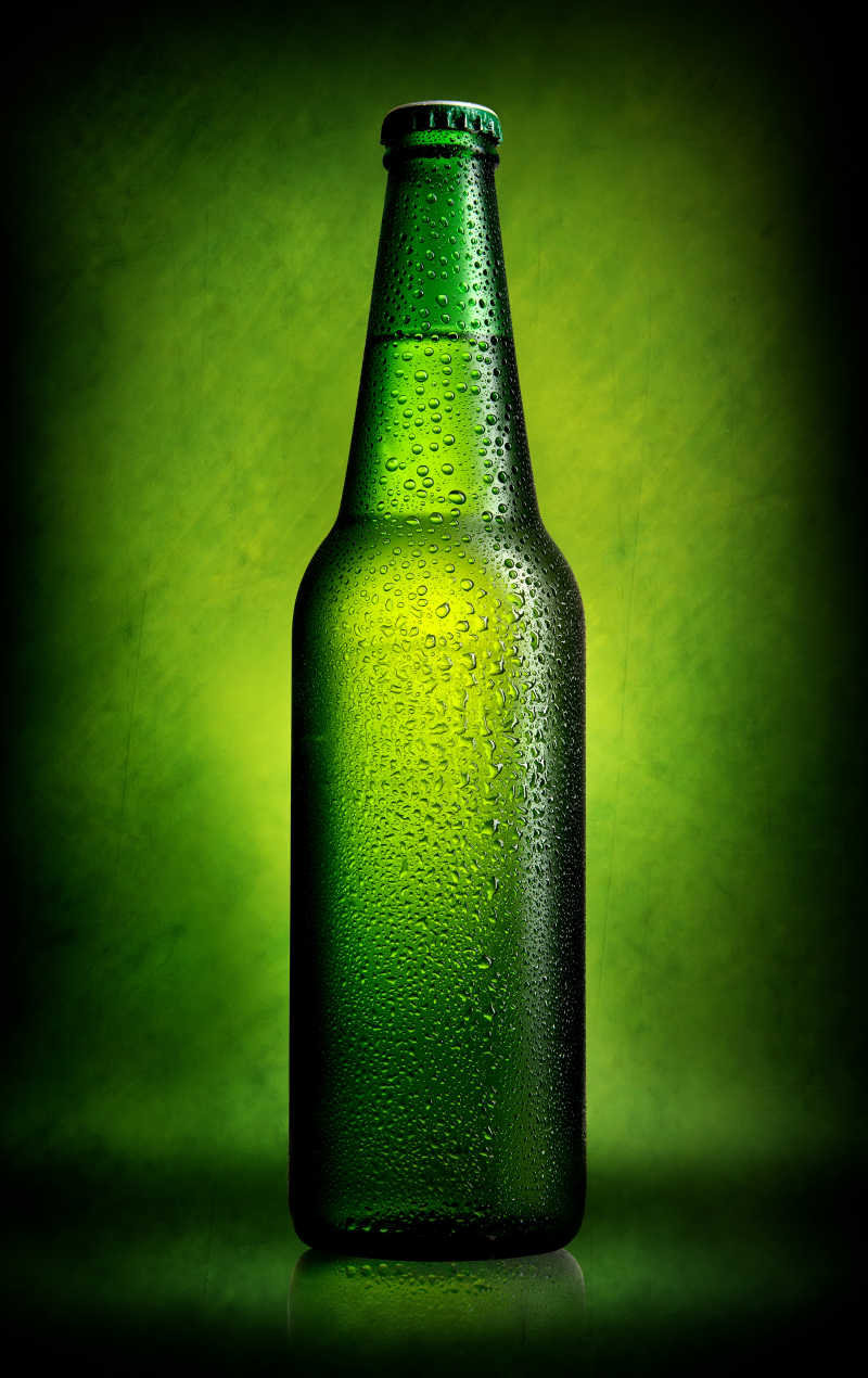 绿色背景上的有水珠的啤酒瓶
