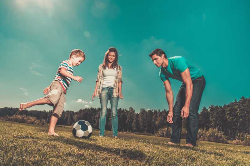 草地上年轻的一家三口一起踢足球