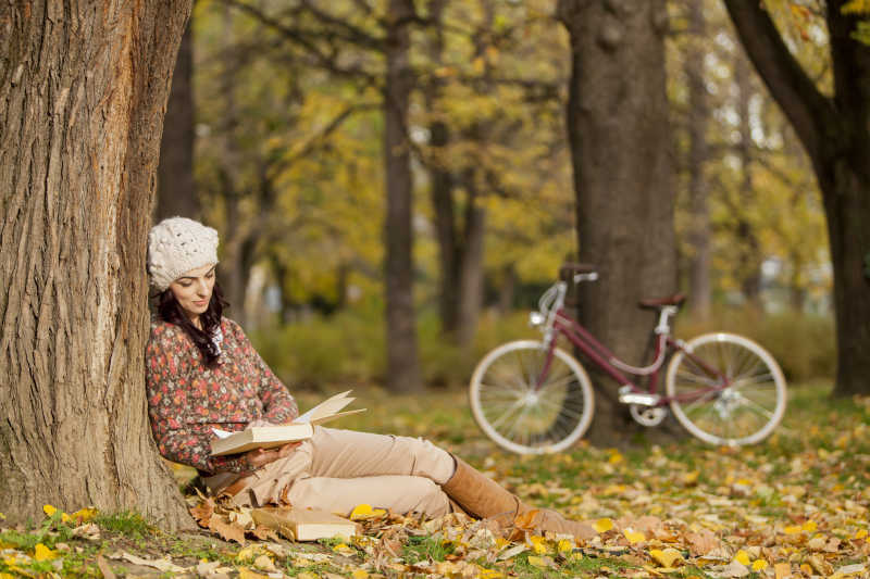 骑行到秋天森林里的女子在树下看书