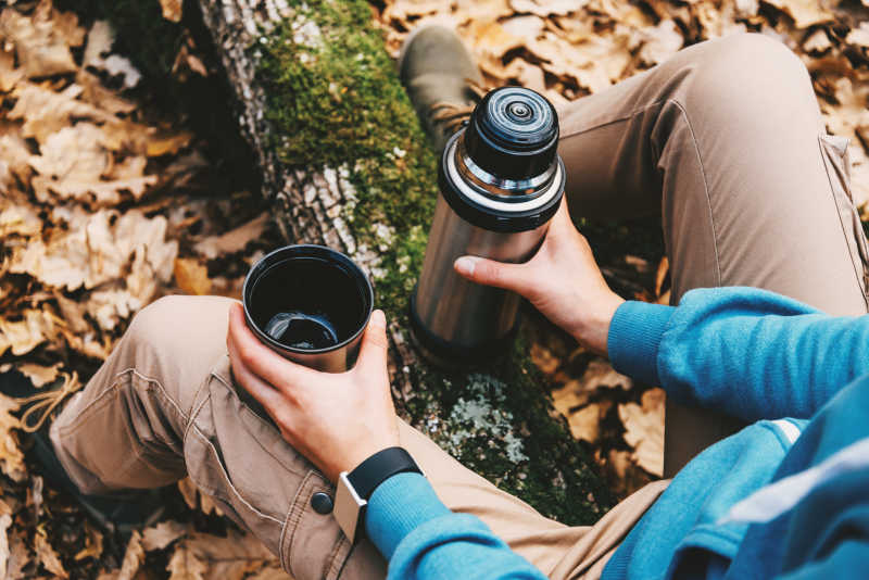 森林里抱着一杯茶和保温瓶的旅行妇女