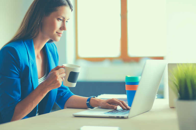 商业女性坐在办公桌旁捧着一杯咖啡