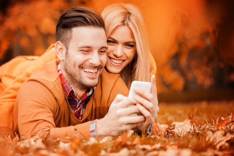 公园里快乐的年轻夫妇看着手机