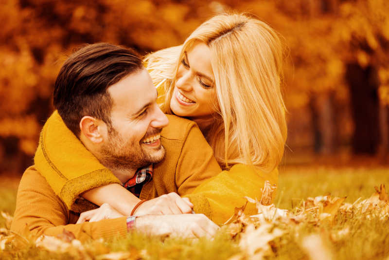 一对微笑的情侣躺在秋天的公园里