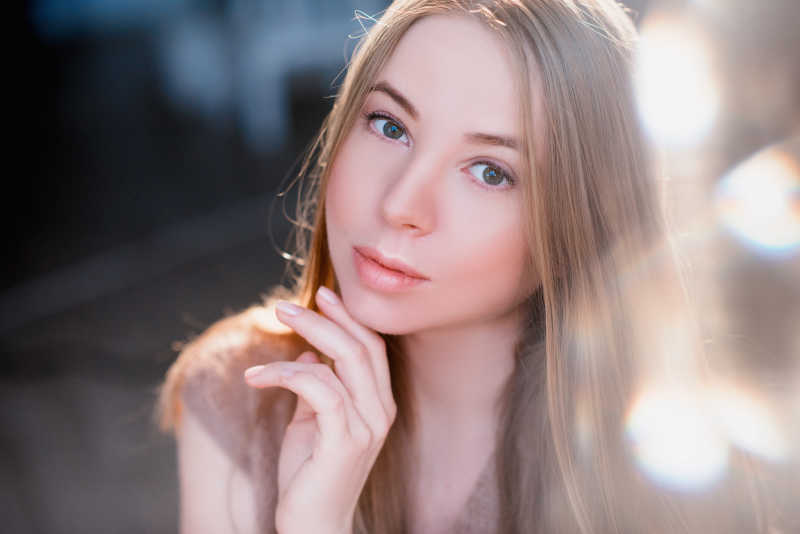 有光斑的天气里用手指托着下巴的美女