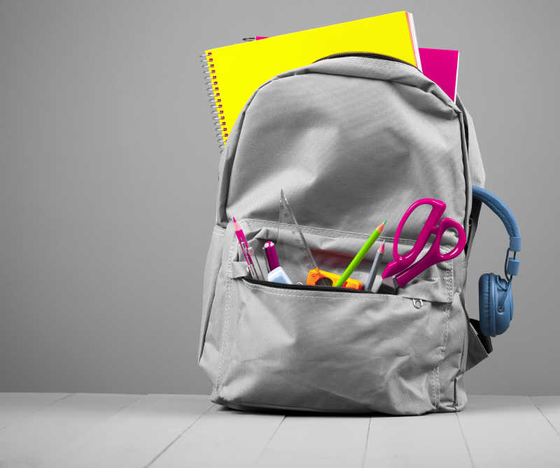 灰色背景下的学校背包中的学习用品