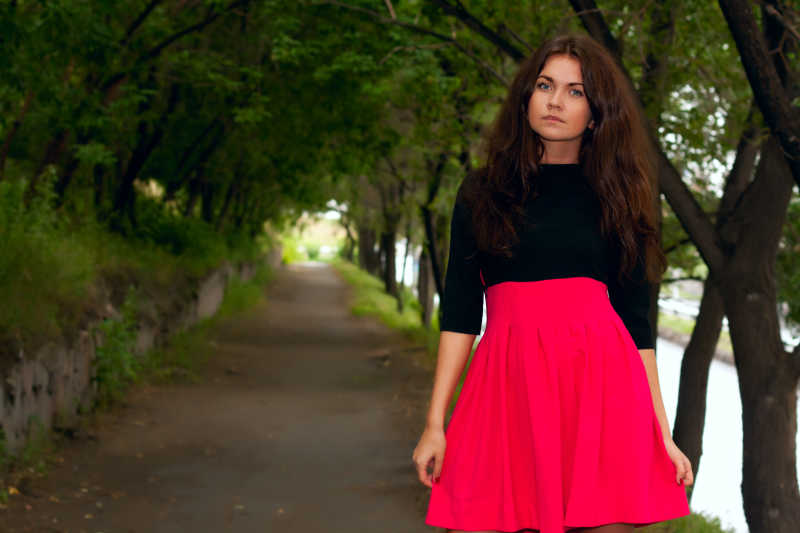 走在公园的小巷的美丽的调情女人穿着红色连衣裙