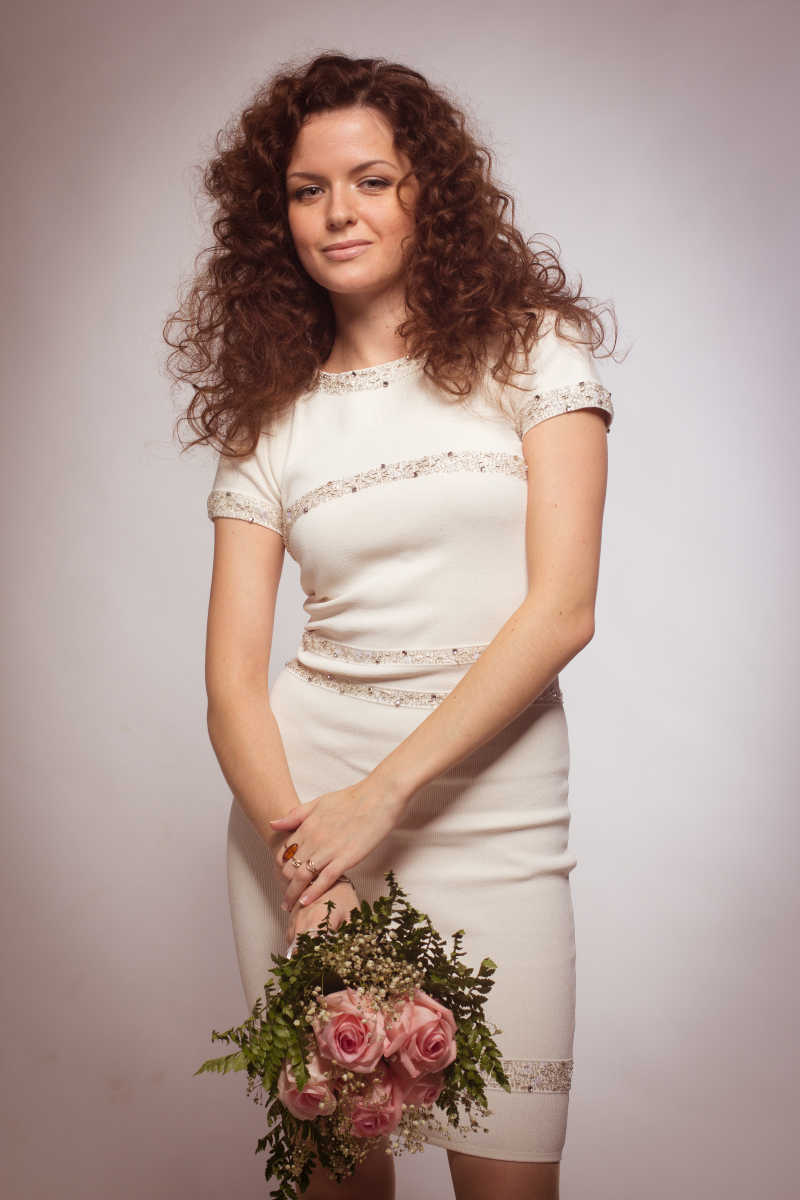 穿着白衣服拿着粉红玫瑰的美丽的白种女人