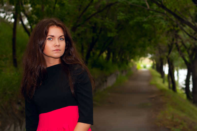 穿着红色连衣裙的美丽的调情女人走在公园的小巷