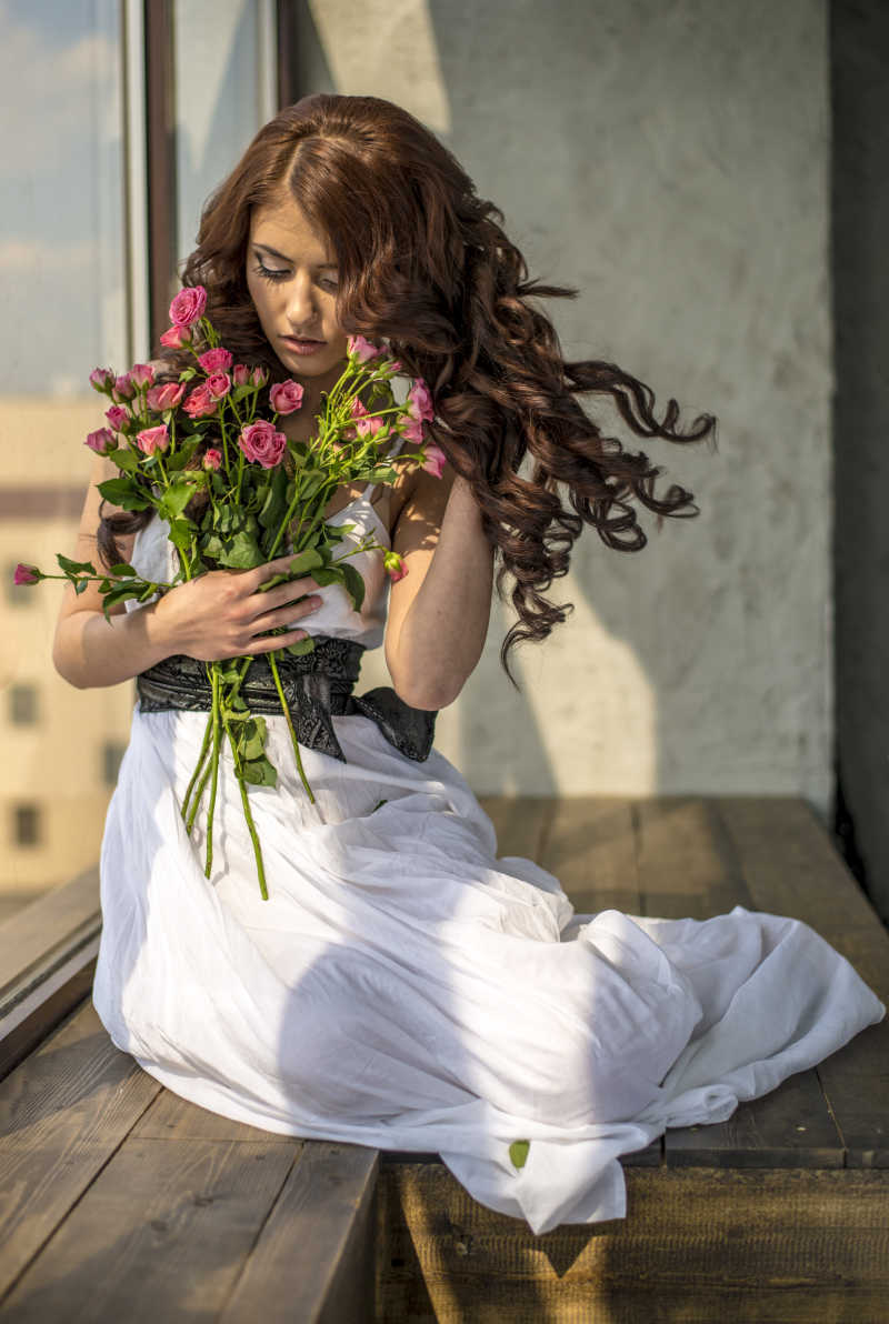 棕色卷发美女穿着长裙拿着花