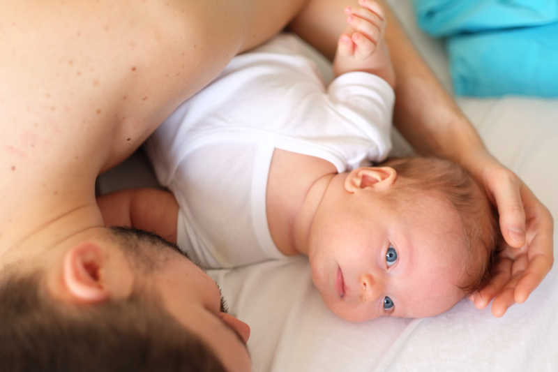 床上在父亲的怀抱里的蓝眼睛的婴儿