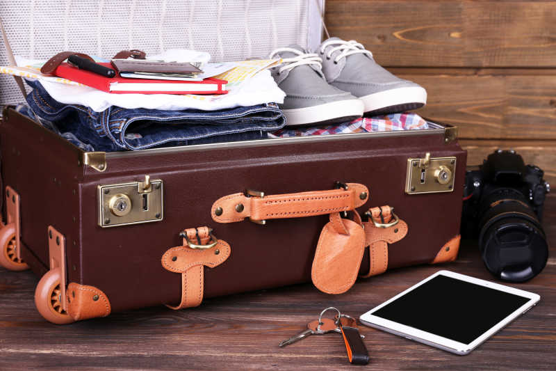 木板上打开的行李箱和照相机平板电脑以及钥匙
