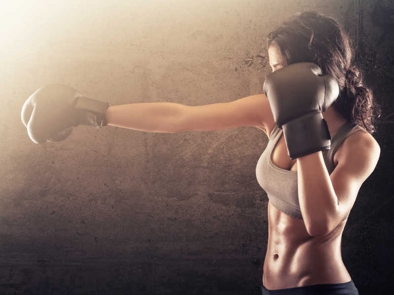 褐色背景下的戴着拳击手套运动的健身美女
