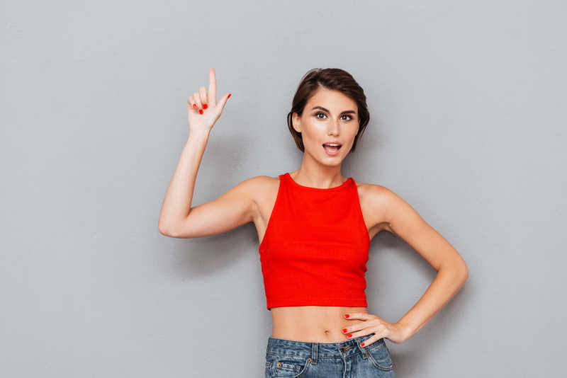 美丽年轻女子用手指指着灰色背景