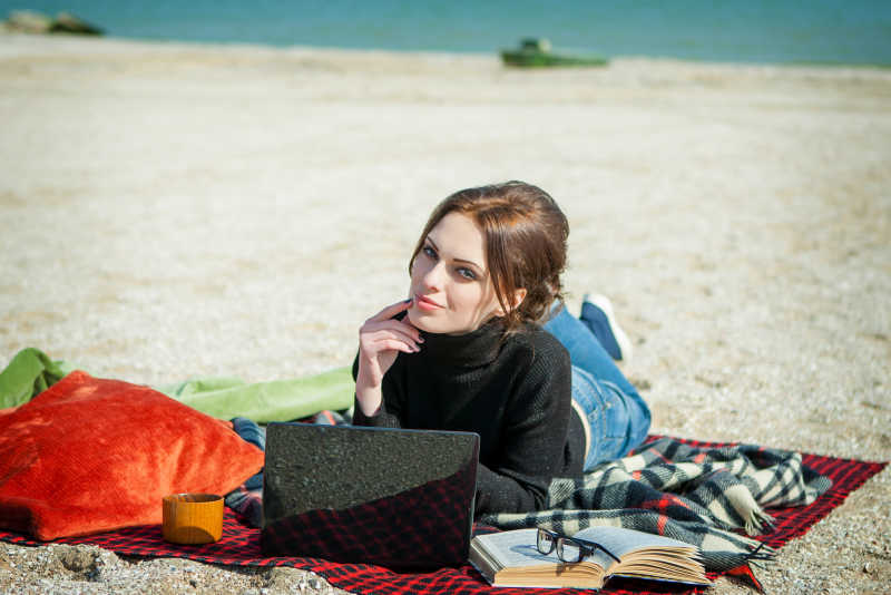 沙滩上趴在笔记本电脑前的年轻女人