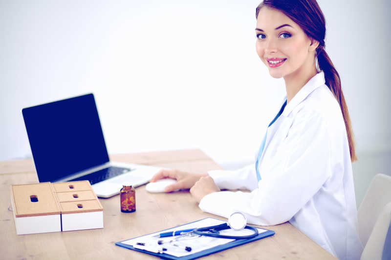 白色背景下坐在办公桌前使用电脑办公的女医生