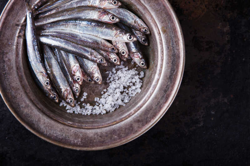 棕色桌上的盘子里的鳀鱼和盐颗粒