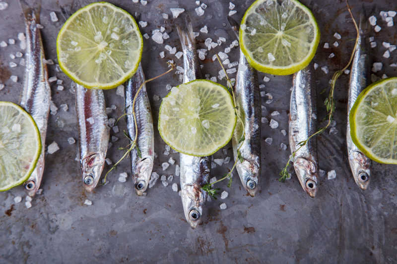 灰色背景上的鳀鱼柠檬片和颗粒状调味料