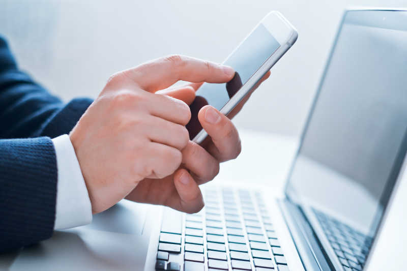 白色背景下男人在有笔记本电脑的办公桌前使用手机