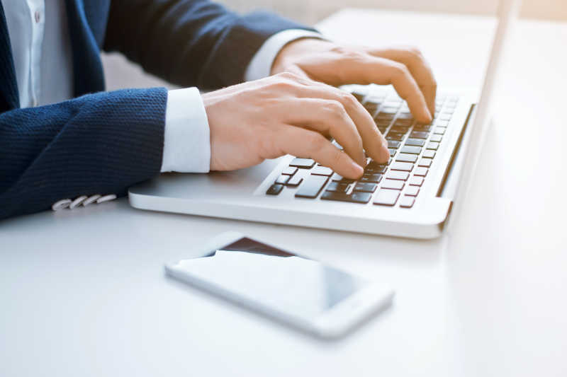 白色桌上双手笔记本电脑上打字的男人