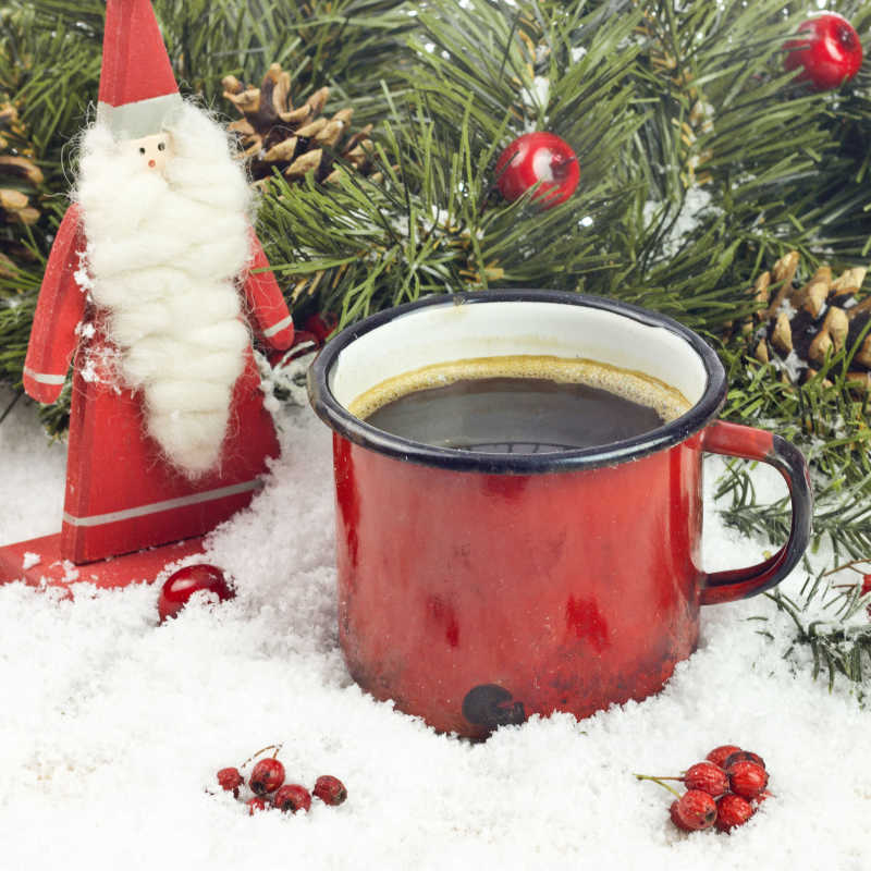 云杉树枝旁放着一杯咖啡和圣诞老人装饰品
