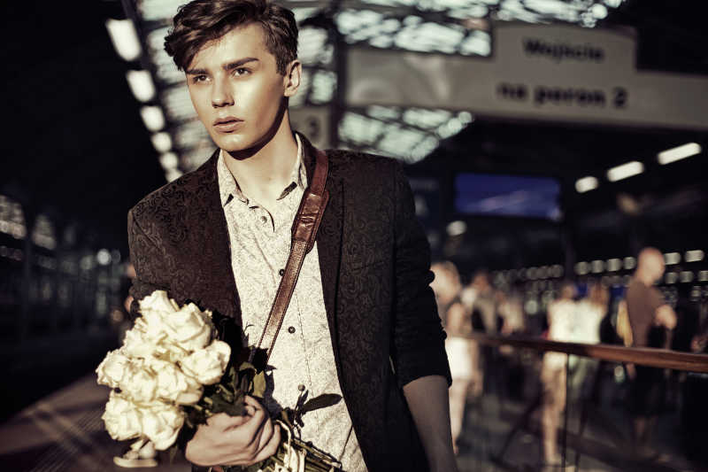 带花的优雅小伙子站在车站里