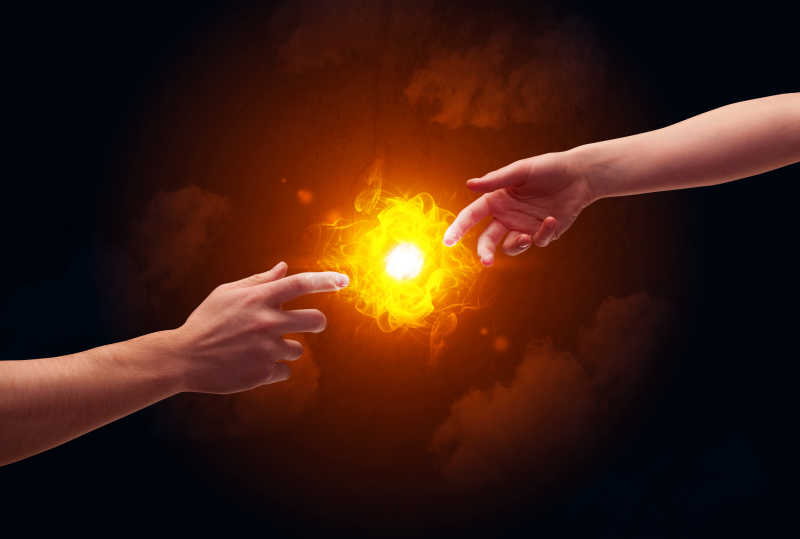 两个赤裸的男人手在触摸着照亮了一个明亮的火焰