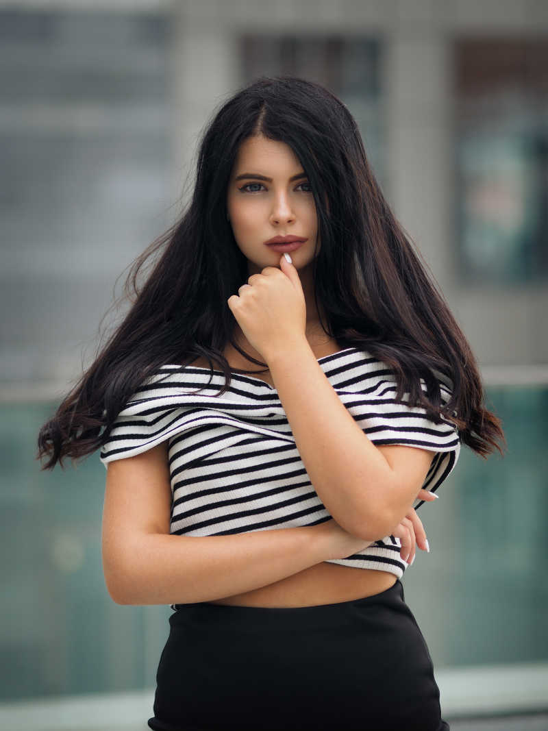 模糊的城市背景下的手撑着下巴的性感黑发美女