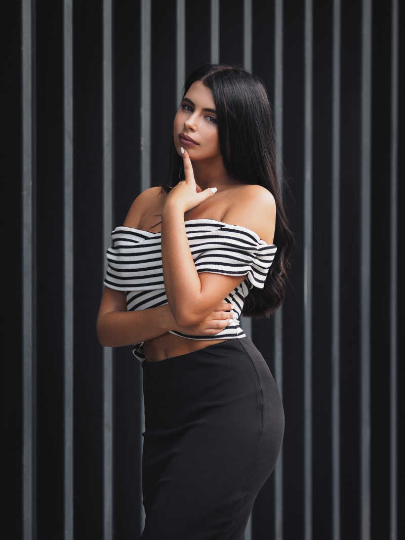  黑白色条纹背景下的手指抚摸着下巴的身材性感的黑发美女