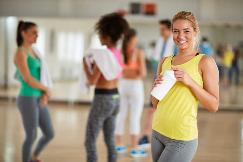 健身房里拿着水杯微笑的金发美女