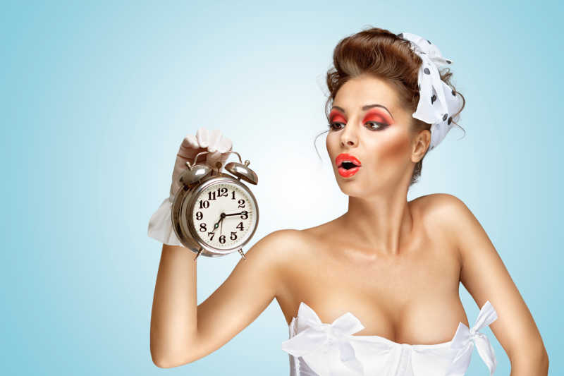 淡蓝色背景下看着手中钟表的化着妆的性感美女