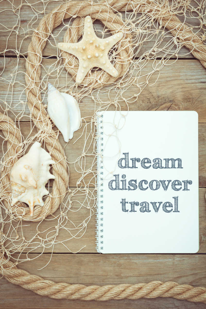 在充满海洋风情的木板上放着一个写着梦发现旅行的本子