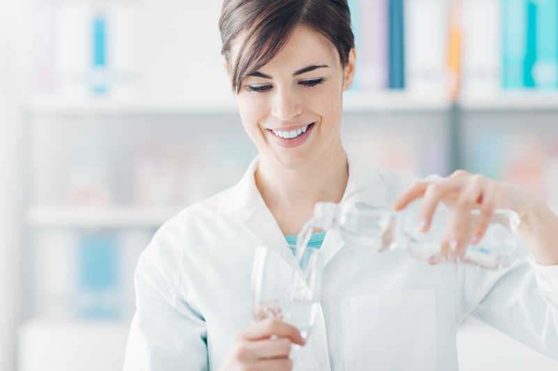 微笑的女医生拿着一瓶水倒进杯子里