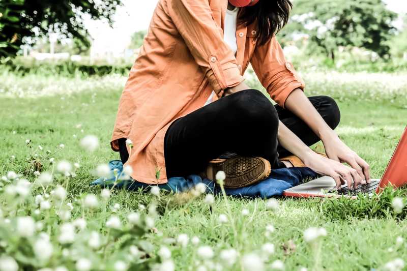 坐在公园草地上使用笔记本电脑的女孩