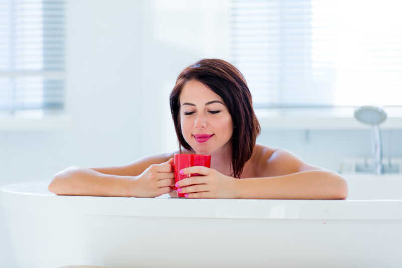 浴室里洗澡喝咖啡的年轻女人