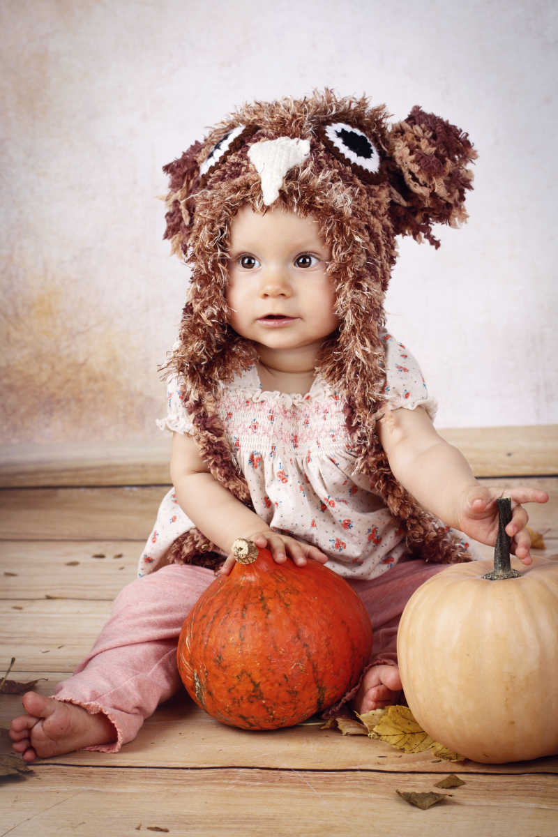 坐在南瓜旁戴着针织帽的漂亮小女孩