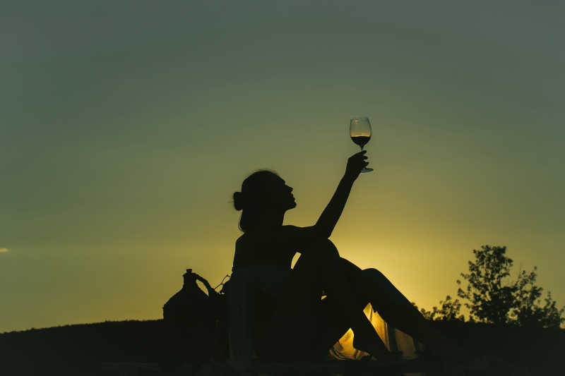 夕阳下举杯喝着葡萄酒的美女剪影