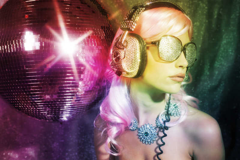 迪斯科球旁边戴着头戴式耳机和墨镜的年轻美女
