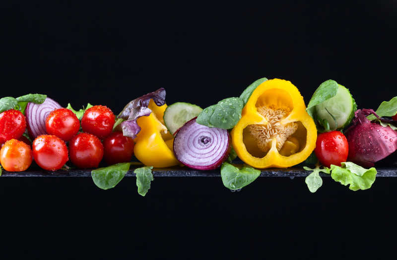 成熟的多汁蔬菜和沙拉叶在黑色背景下