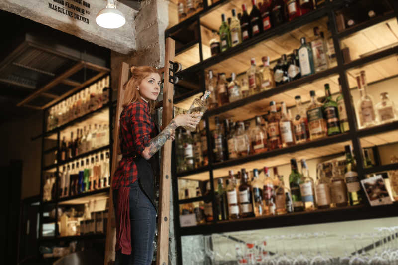 美女从酒吧货架上拿出一瓶酒