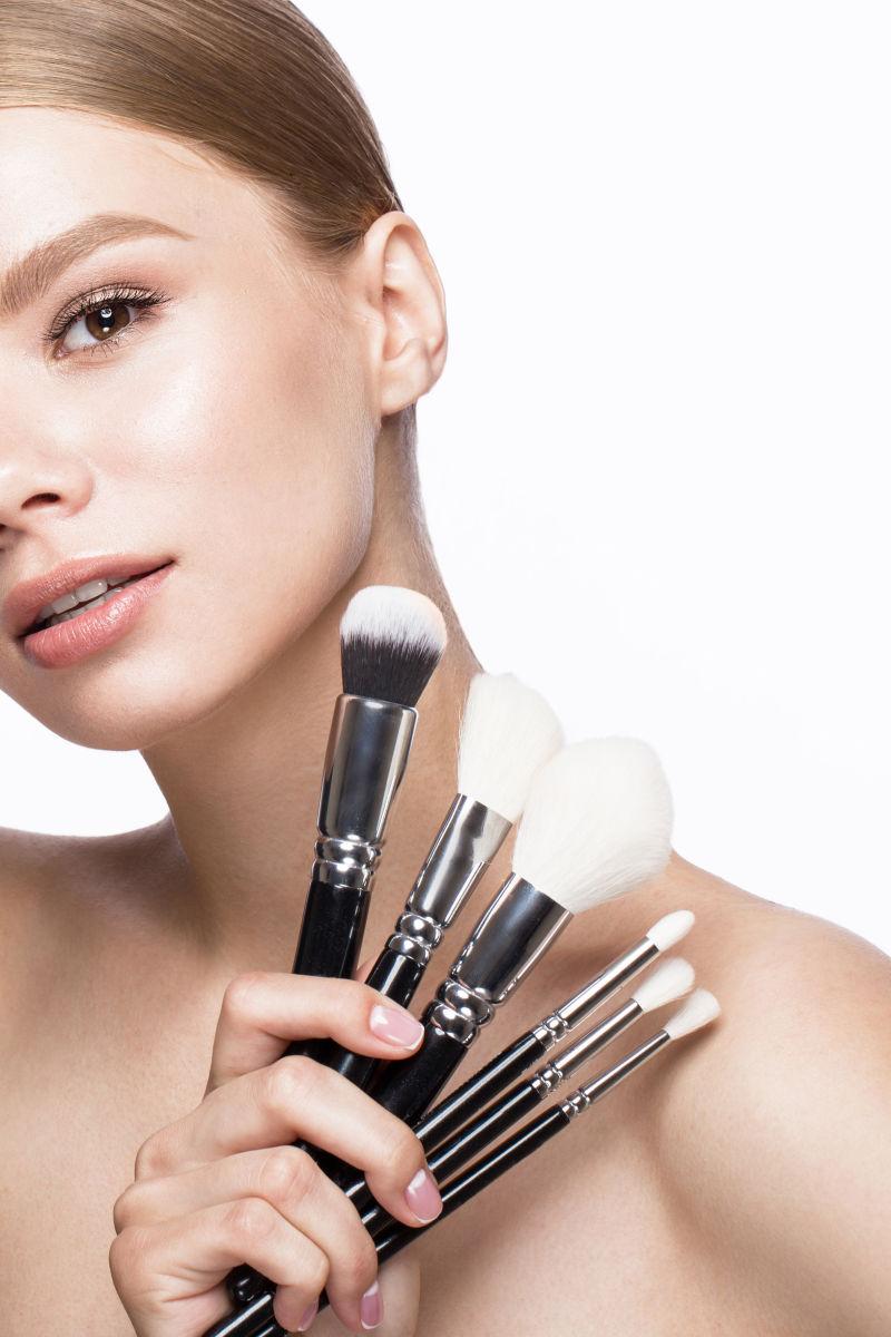 白色背景下展示化妆刷的美女