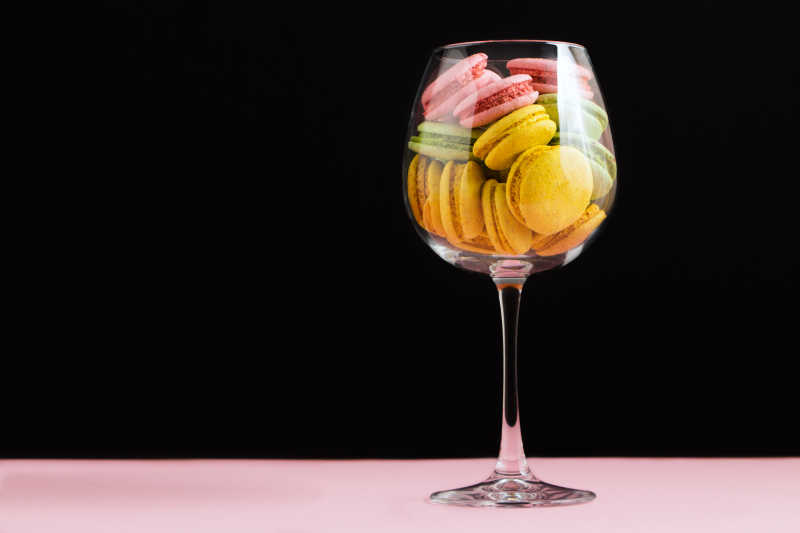 黑色背景下酒杯上的多色马卡龙