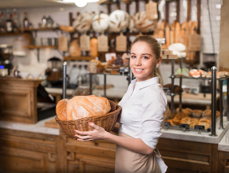 面包店背景下的托着装有面包的篮子的美女