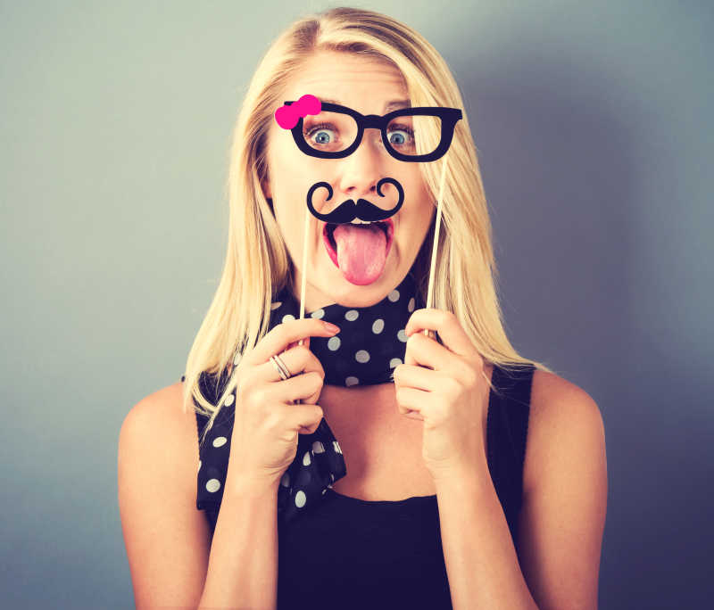 灰色背景下握住纸党棍棒的搞怪年轻女子