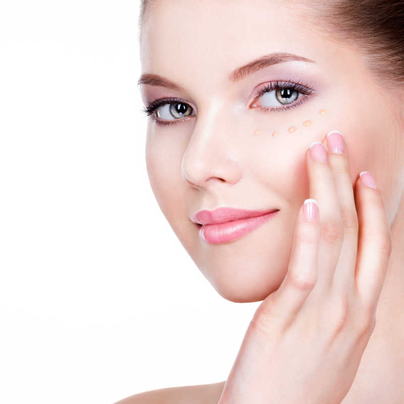 白色背景下眼睛周围涂抹护肤品抚摸自己面部的美女