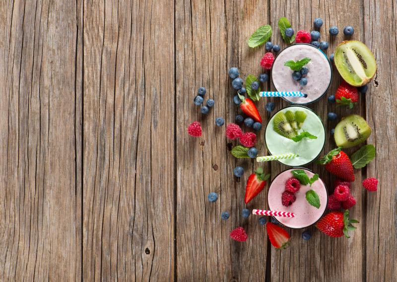 木桌上的不同的浆果和三杯浆果奶昔