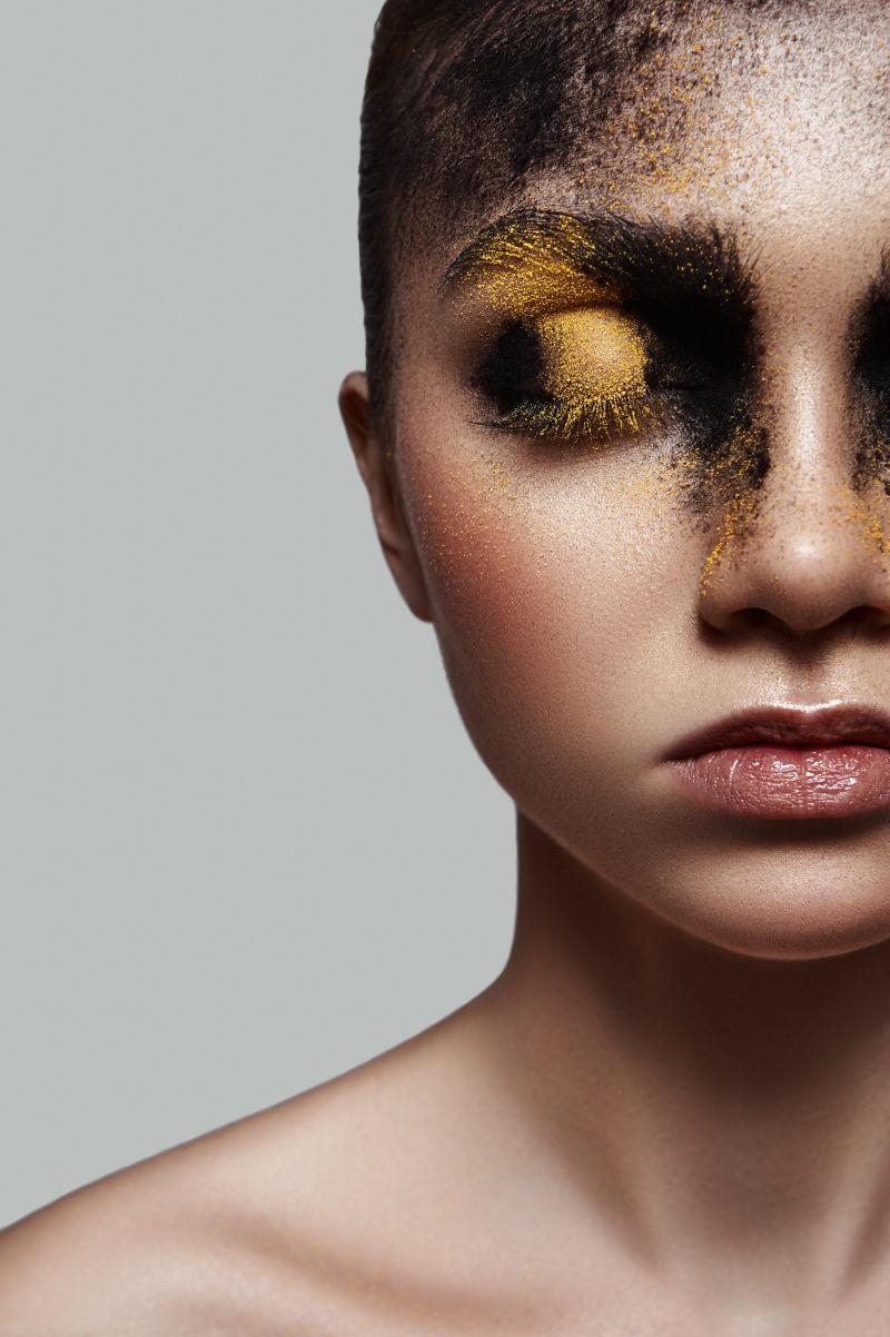灰色背景下眼睛上涂着浓重的黑黄粉的年轻女模特