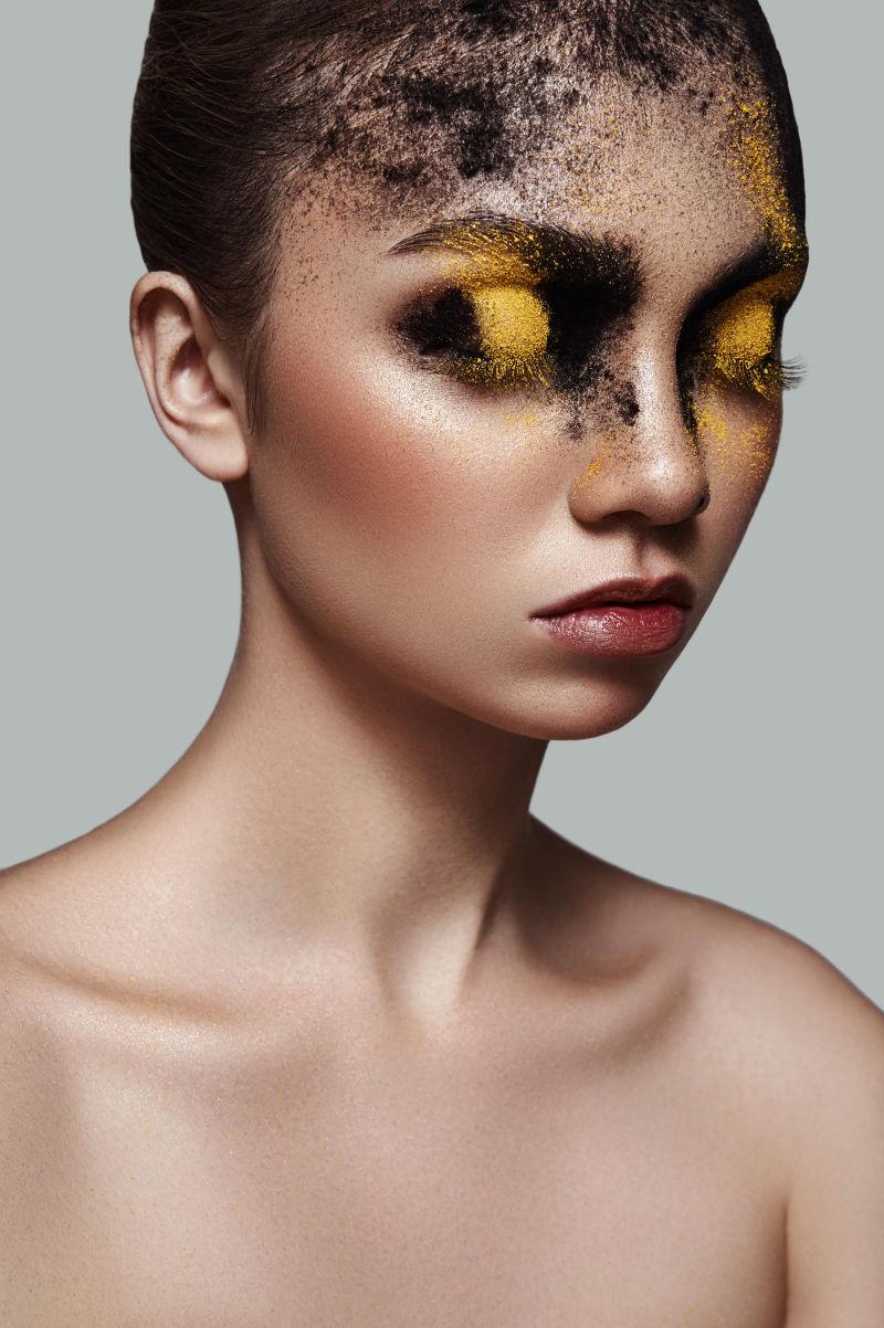 灰色背景下闭着眼睛涂着浓重的黑黄粉的女模特