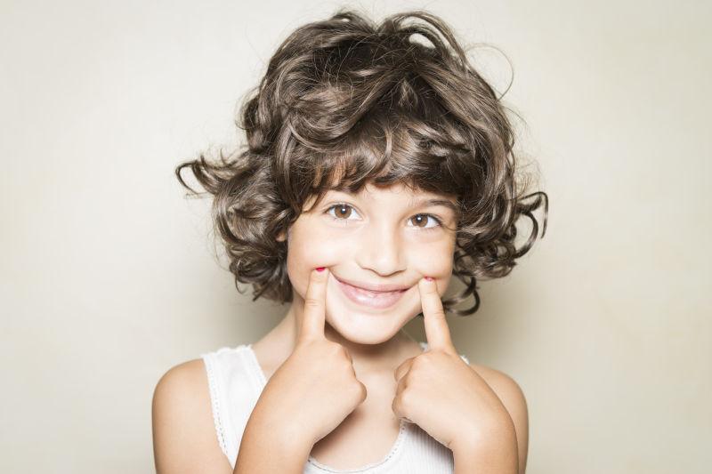 可爱的卷发小女孩的微笑手势