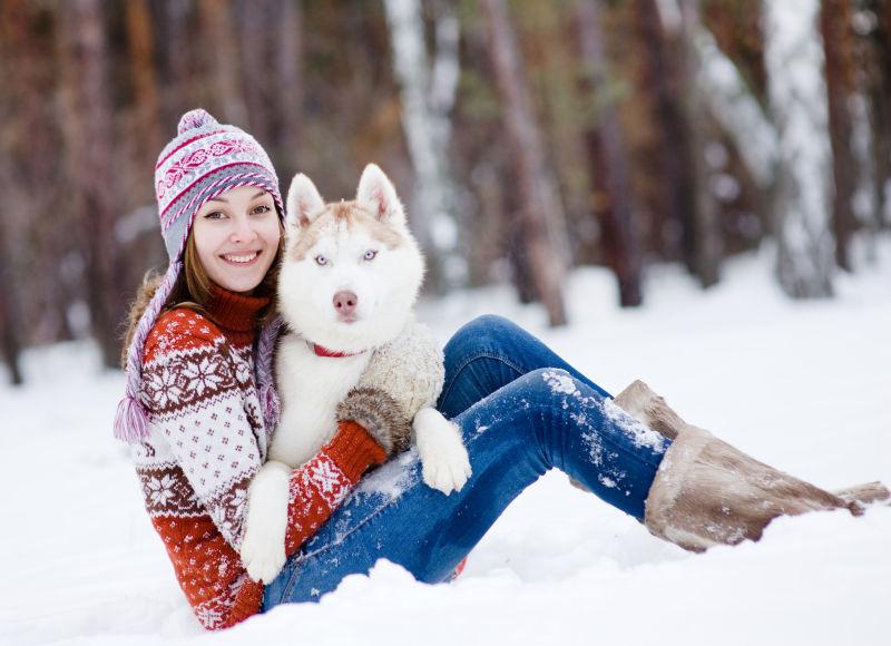 做在雪地上的快乐女孩和哈士奇