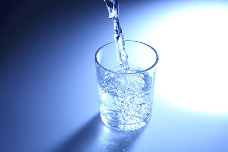 蓝光背景下倒入水杯中的清水